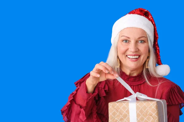 色の背景にクリスマスの贈り物を持つ高齢女性 — ストック写真