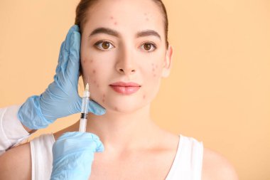 Akne sorunu olan genç bir kadın yüzüne renk arka planına karşı iğne vuruluyor.