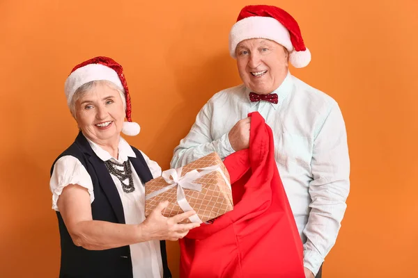 色の背景にクリスマスの贈り物と高齢者のカップル — ストック写真