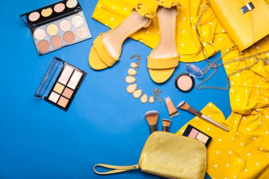 Renkli arka planda dekoratif kozmetik ürünleri, kıyafetler ve aksesuarlar bulunan makyaj çantası