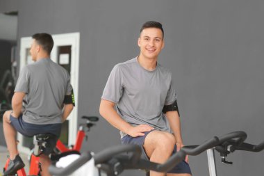 Genç adam spor salonunda egzersiz bisikleti eğitimi alıyor.