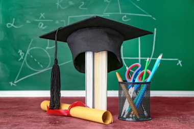 Mezuniyet şapkası, diploma ve kırtasiye malzemeleri sınıftaki masada.