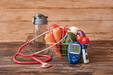 Sebzeli alışveriş arabası, steteskop, tükenmez kalem ve tahta arka planda glukometre. Diyabet kavramı