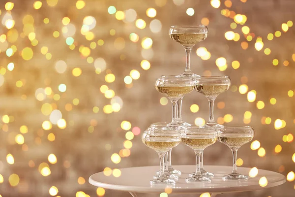 Tower made of glasses with champagne on table against blurred lights