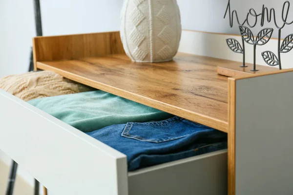 Modern chest of drawers with clothes in room, closeup