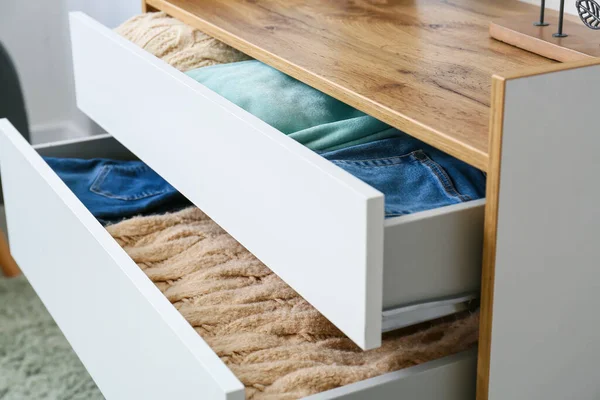 Modern chest of drawers with clothes in room, closeup