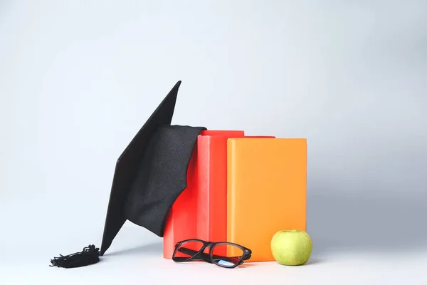 Graduation hat, eyeglasses and books on light background