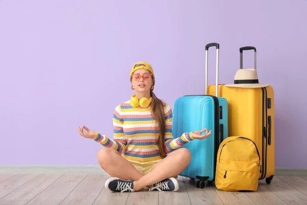 Young woman with luggage meditating near color wall. Travel concept