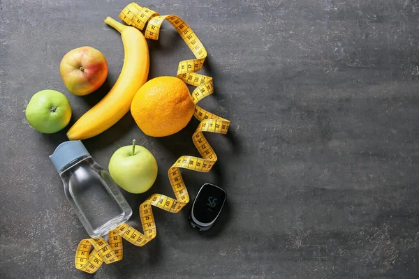 Fruits, measuring tape and bottle of water and glucometer on dark background. Diabetes concept