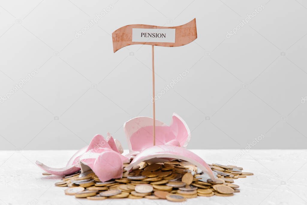 Broken piggy bank with coins and word PENSION on table