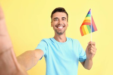 LGBT bayrağı taşıyan genç adam arka planda selfie çekiyor.