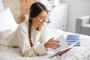 Evde kitap okuyan güzel genç bir kadın.