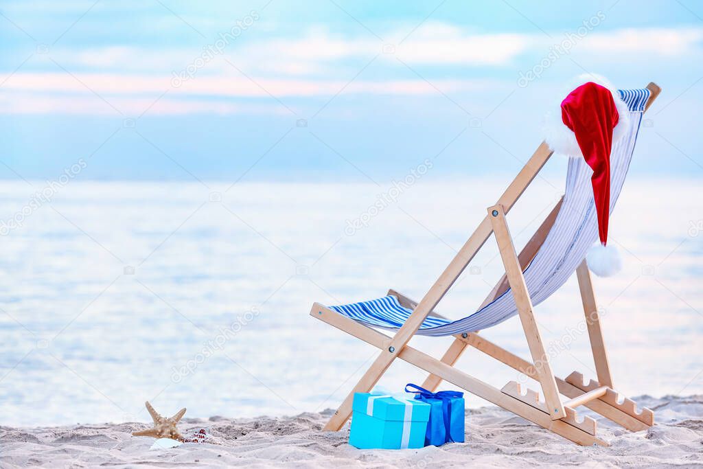 Beach chair, gifts and Santa hat on sea shore. Christmas vacation concept