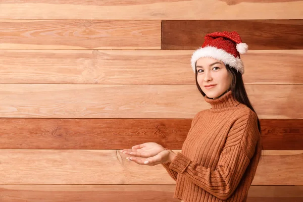 Krásná Mladá Žena Santa Klobouk Ukazuje Něco Dřevěném Pozadí — Stock fotografie