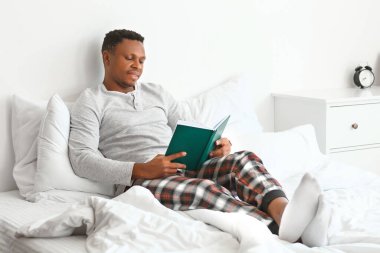 Afro-Amerikalı adam evde kitap okuyor.