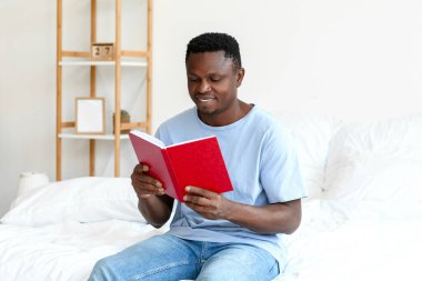 Afro-Amerikalı adam evde kitap okuyor.