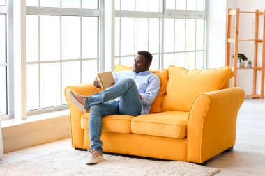 Afro-Amerikalı adam evde kitap okuyor.