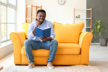 Afro-Amerikalı adam evde kitap okuyor.