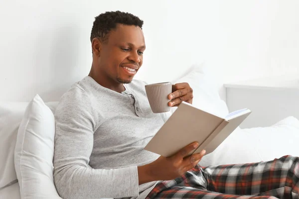 African-American man reading book and drinking coffee at home