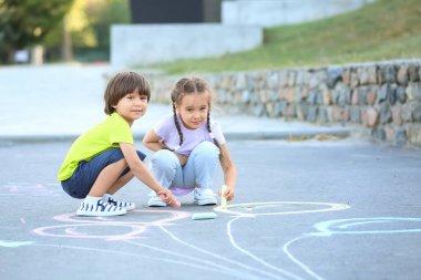 Küçük çocuklar asfalta tebeşirle resim çiziyor.