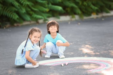 Küçük çocuklar asfalta tebeşirle resim çiziyor.