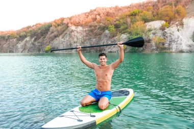 Genç adam nehirde sörf yapmak için sörf tahtası kullanıyor.