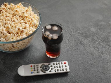 Gri arka planda lezzetli patlamış mısır, kola ve televizyon uzaktan kumandası