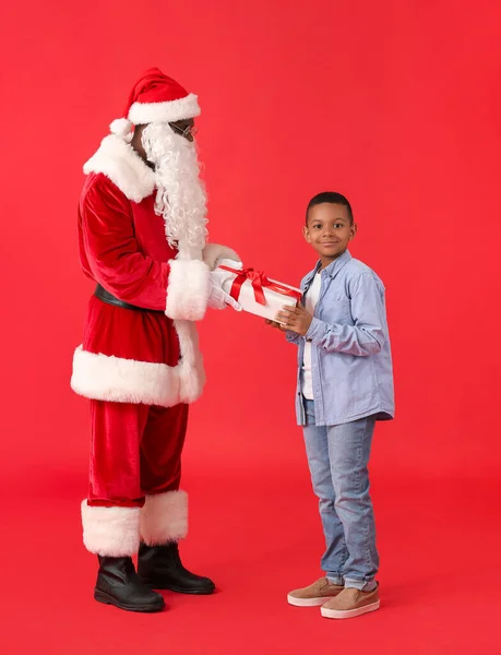 アフリカ系アメリカ人サンタクロースは 色の背景にかわいい男の子にプレゼント — ストック写真