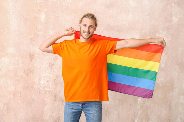 Young man with LGBT flag on color background