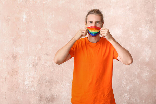 Young man in rainbow mask on color background. LGBT concept