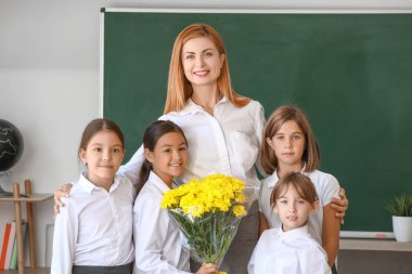 Öğretmenli okul çocukları ve sınıfta bir buket çiçek.
