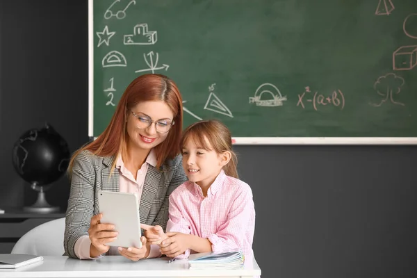 Teacher with little schoolgirl with tablet computer in classroom