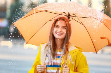 Şemsiyeli güzel genç bir kadın açık havada yağmurluk giyiyor