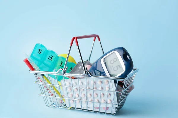 Shopping basket with glucometer, pills and syringes on color background. Diabetes concept