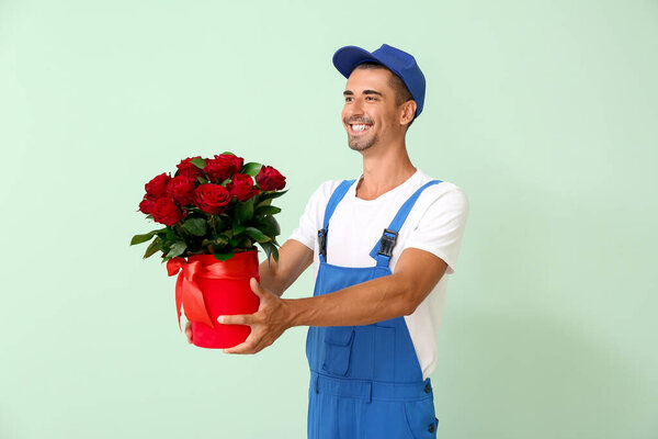 Delivery man with bouquet of flowers on color background