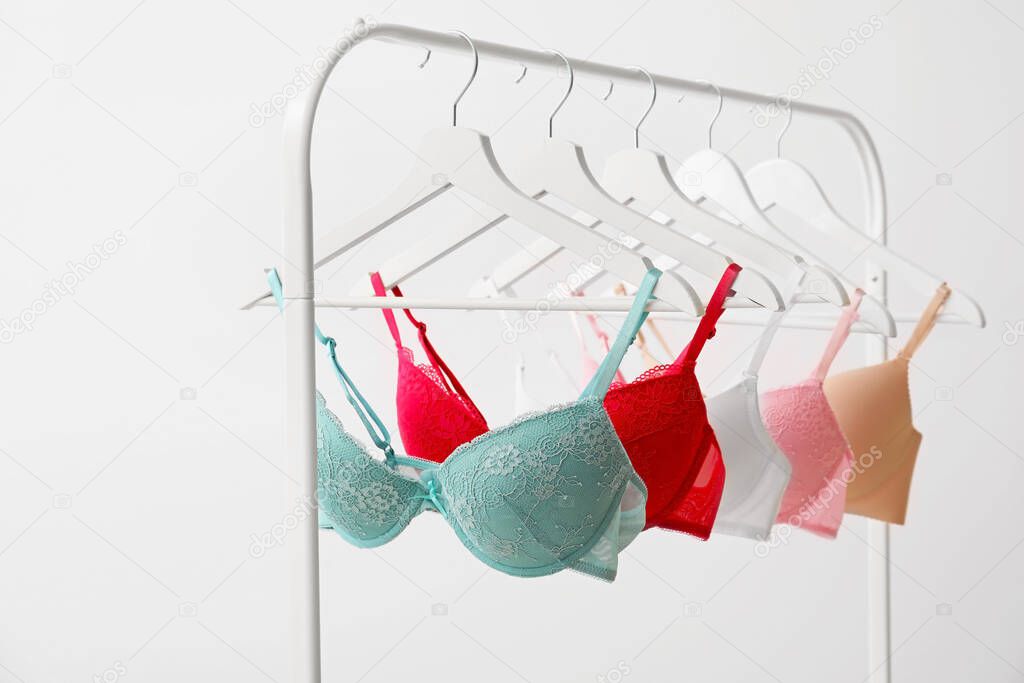 Clothes rack with stylish bras on light background