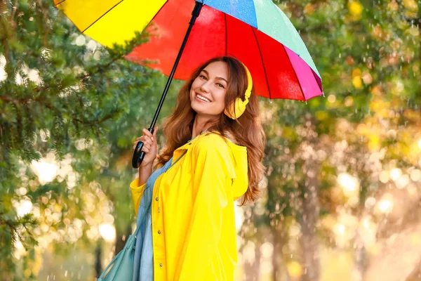 Beautiful young woman with umbrella wearing raincoat in park