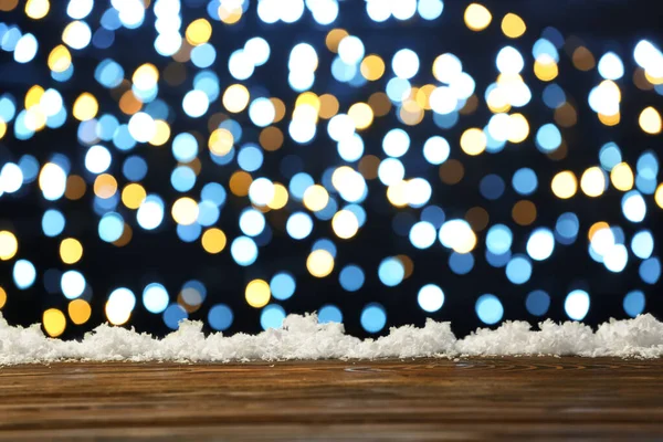 Empty wooden table with snow against blurred Christmas lights