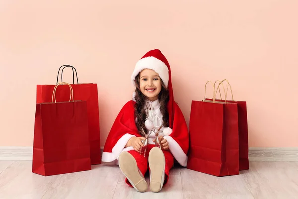 漂亮的小女孩穿着圣诞老人的服装 带着购物袋靠近彩墙 — 图库照片