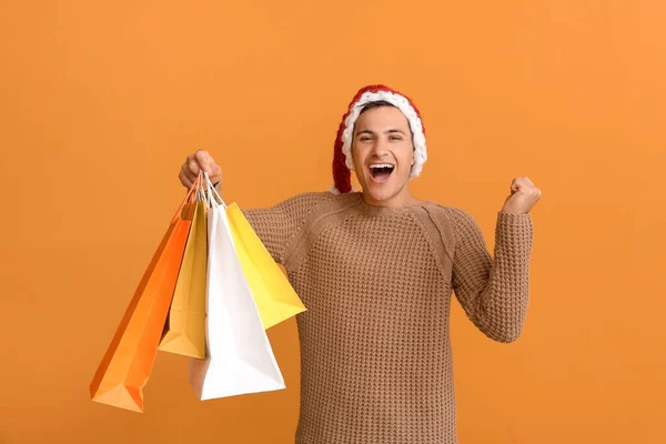 Glücklicher Mann Mit Weihnachtsmütze Und Mit Einkaufstaschen Auf Farbigem Hintergrund — Stockfoto