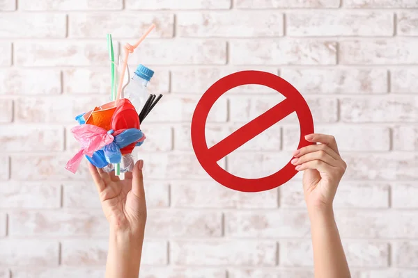 Female hands with plastic garbage and stop sign on brick background. Ecology concept