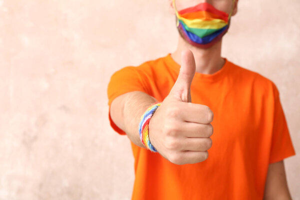 Young man in rainbow mask showing thumb-up on color background. LGBT concept