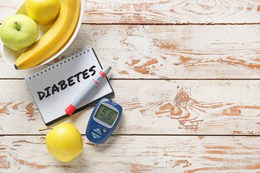 Meyveler, diABETES yazılı defter, beyaz tahta zemin üzerinde lamba kalem ve glukometre
