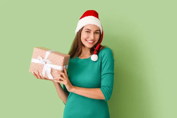 サンタの帽子の美しい若い女性と色の背景の贈り物 — ストック写真