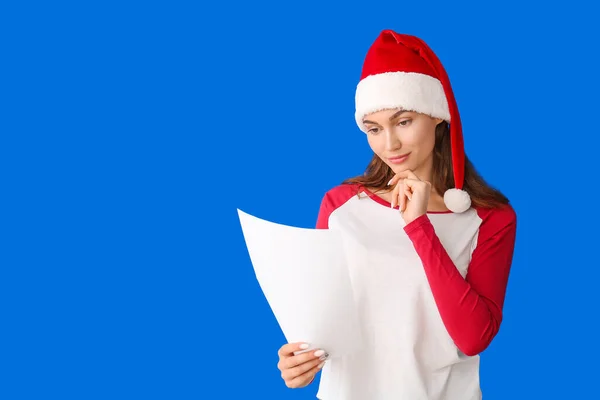 stock image Beautiful young woman in Santa hat reading letter on color background