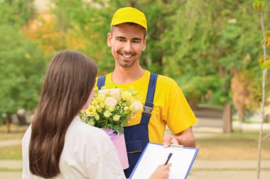 Dışarıdaki teslimatçıdan güzel çiçekler alan genç bir kadın.