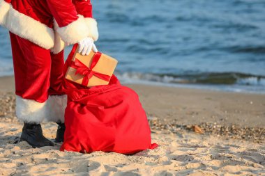 Noel Baba Noel hediyelerini kumsalda çantasında taşıyor.