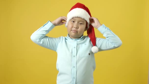 可爱的亚洲男孩把他的圣诞老人的帽子与色彩背景相对照 — 图库视频影像