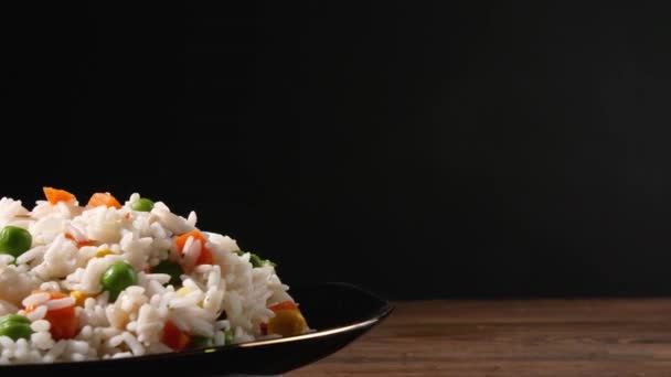 用煮过的米饭和蔬菜在深色背景下在桌子上旋转的盘子 — 图库视频影像