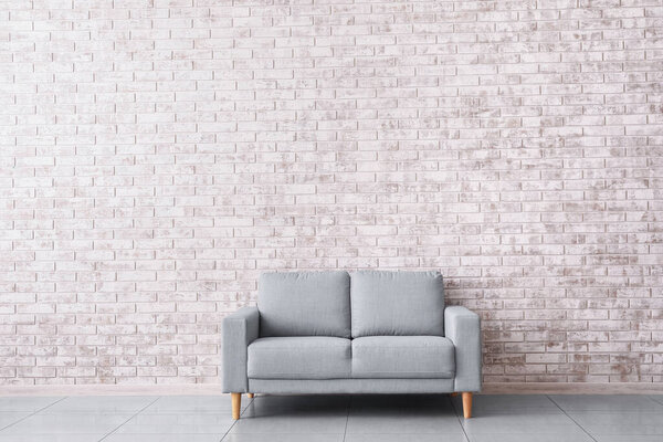 Stylish sofa near brick wall in room